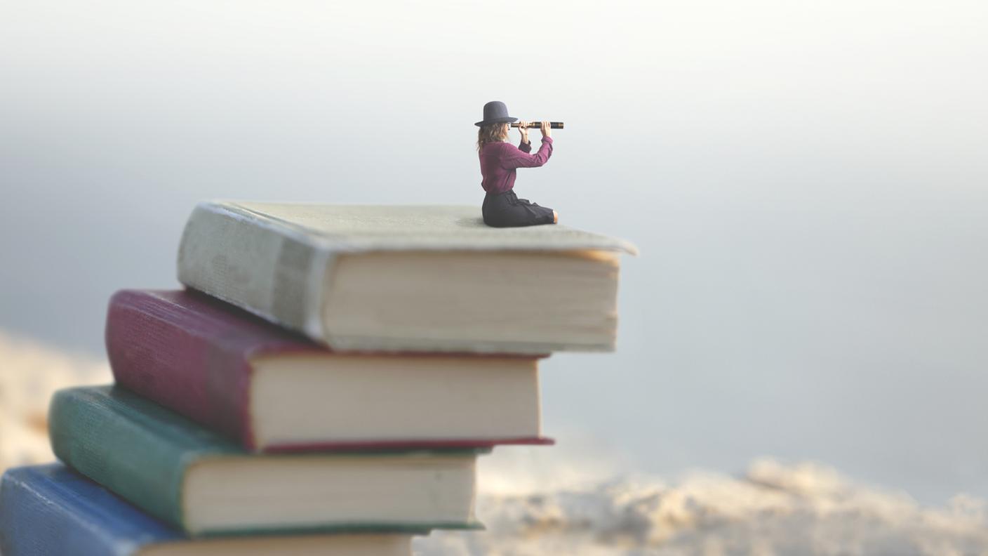 Donna seduta su dei giganti libri osserva con un binocolo l'orizzonte