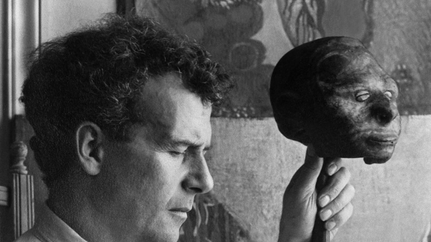 L'artista e pittore svizzero Serge Brignoni con una scultura in legno davanti a un quadro