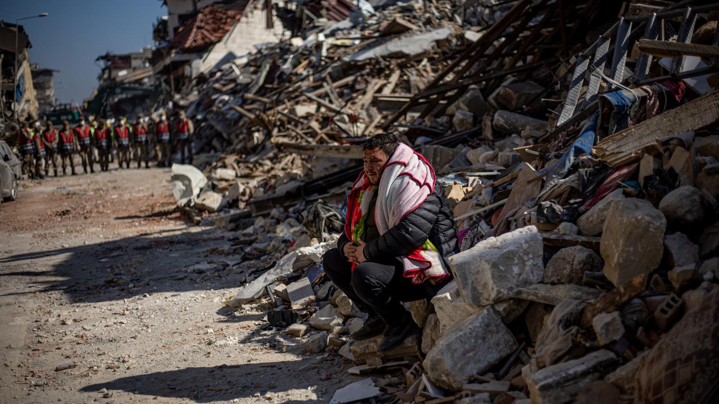 Un uomo siede sulle macerie di edifici crollati dopo il potente terremoto, a Hatay, Turchia.