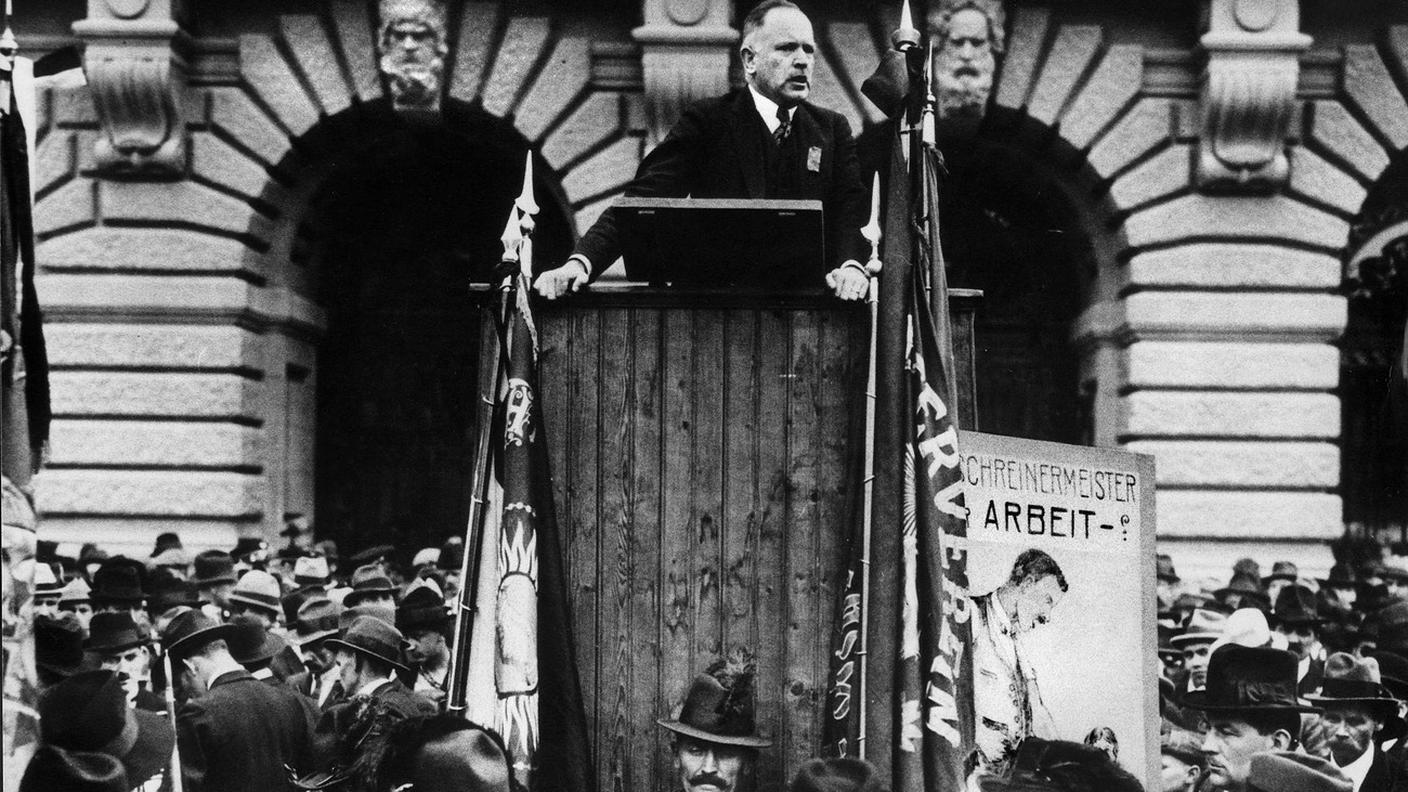 Keystone Robert Grimm tiene un discorso davanti al Palazzo federale (sede del governo e del parlamento) a Berna, in Svizzera, ca. 1920. Il parlamentare della SP era una persona molto influente nei circoli politici di sinistra a Berna e in Svizzera in generale nella prima metà del XX secolo. Fu autore del bando per uno sciopero generale nel 1918. In esso chiedeva riduzioni di prezzo, rappresentanza proporzionale e diritto di voto delle donne, introduzione della settimana lavorativa di 48 ore e pensione di anzianità. 