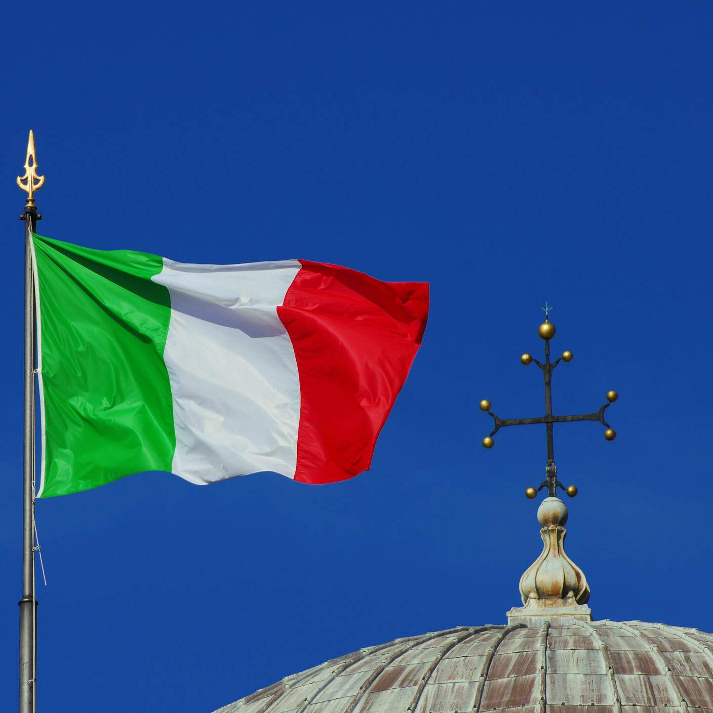 Bandiera Nazionale Italiana sventolante al vento vicino a un croce cristiana