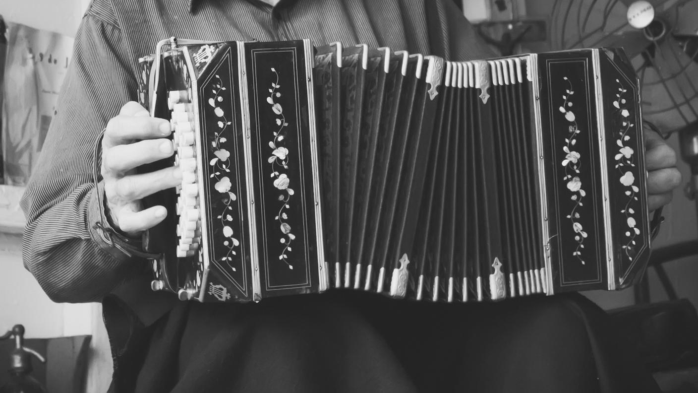 Buenos Aires, Argentina - April 15, 2015: A black and white image of Norberto Gradilone playing tango music the bandoneon in a typical Argentine conventillo in the La Boca neighborhood of Buenos Aires. He is often seen playing here on Caminito Street.