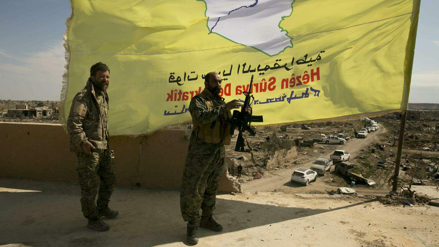 Soldati delle Forze Democratiche Siriane in posa davanti alla loro bandiera