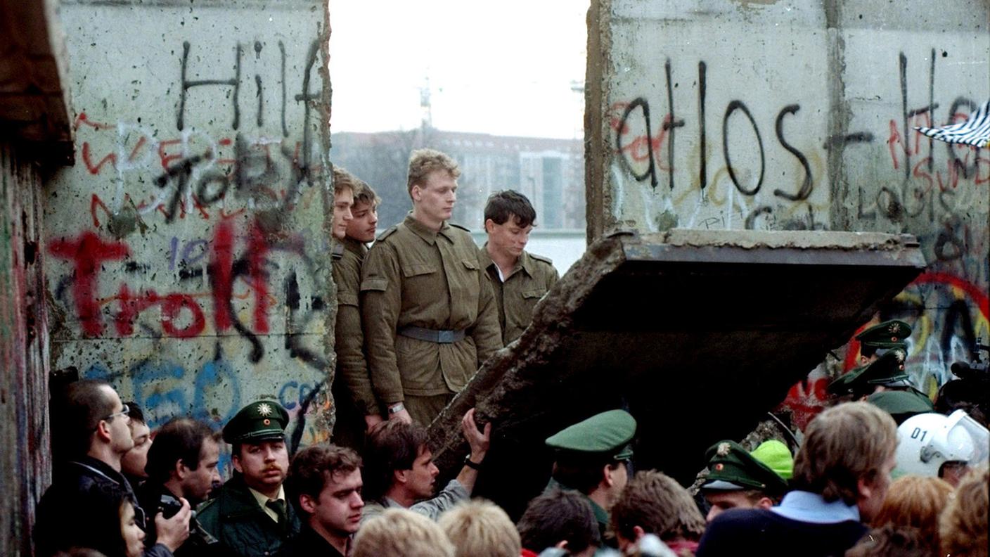 Le guardie di frontiera della DDR guardano la caduta di un segmento del muro di Berlino, 9 novembre 1989