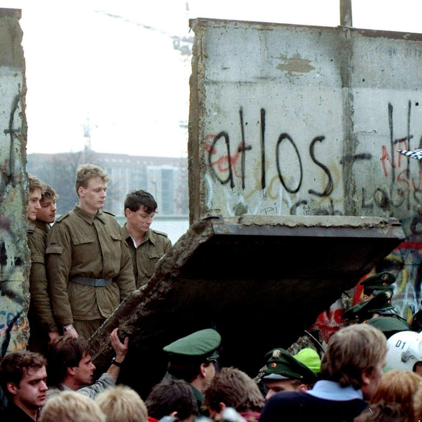 Le guardie di frontiera della DDR guardano la caduta di un segmento del muro di Berlino, 9 novembre 1989