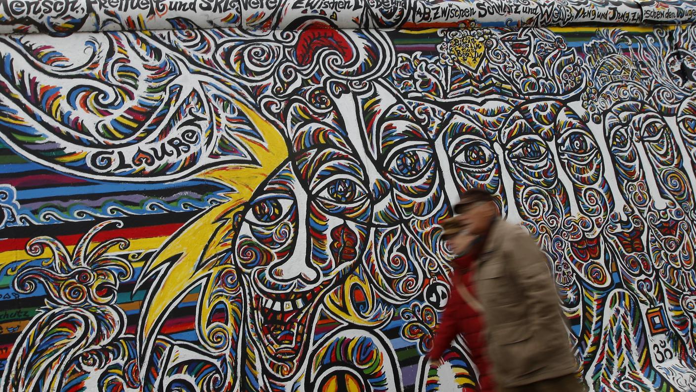 La gente cammina lungo il tratto restaurato della East Side Gallery, la più grande parte rimasta dell'ex muro di Berlino