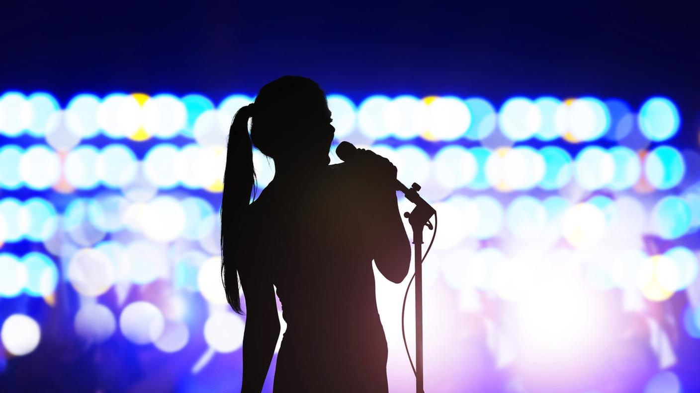 silhouette di donna con microfono che canta sul palco del concerto davanti alla folla
