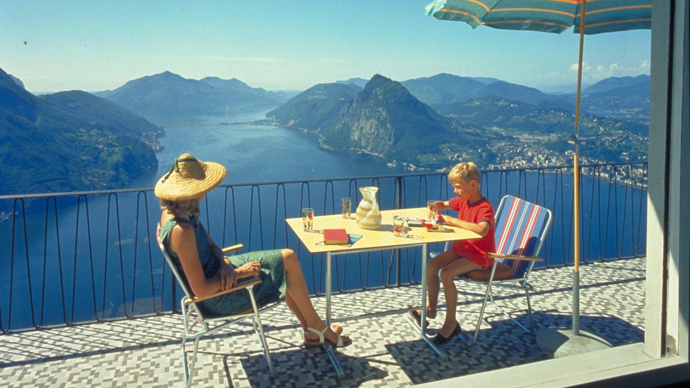 I turisti della Svizzera tedesca e del Nord Europa sono attratti in Ticino dal clima mite e dalla bellezza del paesaggio. Le case di vacanza vengono acquistate qui alla ricerca di un investimento sicuro. Vista del lago di Lugano dalla finestra di una casa di vacanza. Brè su Lugano / TI, 1964-1965