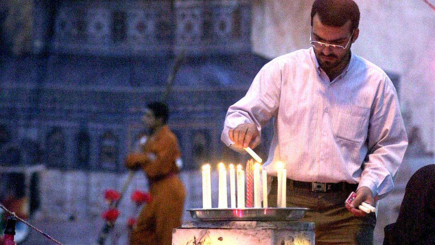 Un uomo iraniano accende candele durante una messa in memoria delle persone uccise nei Territori palestinesi di fronte a un murale del defunto leader spirituale iraniano Ayatollah Khomeini