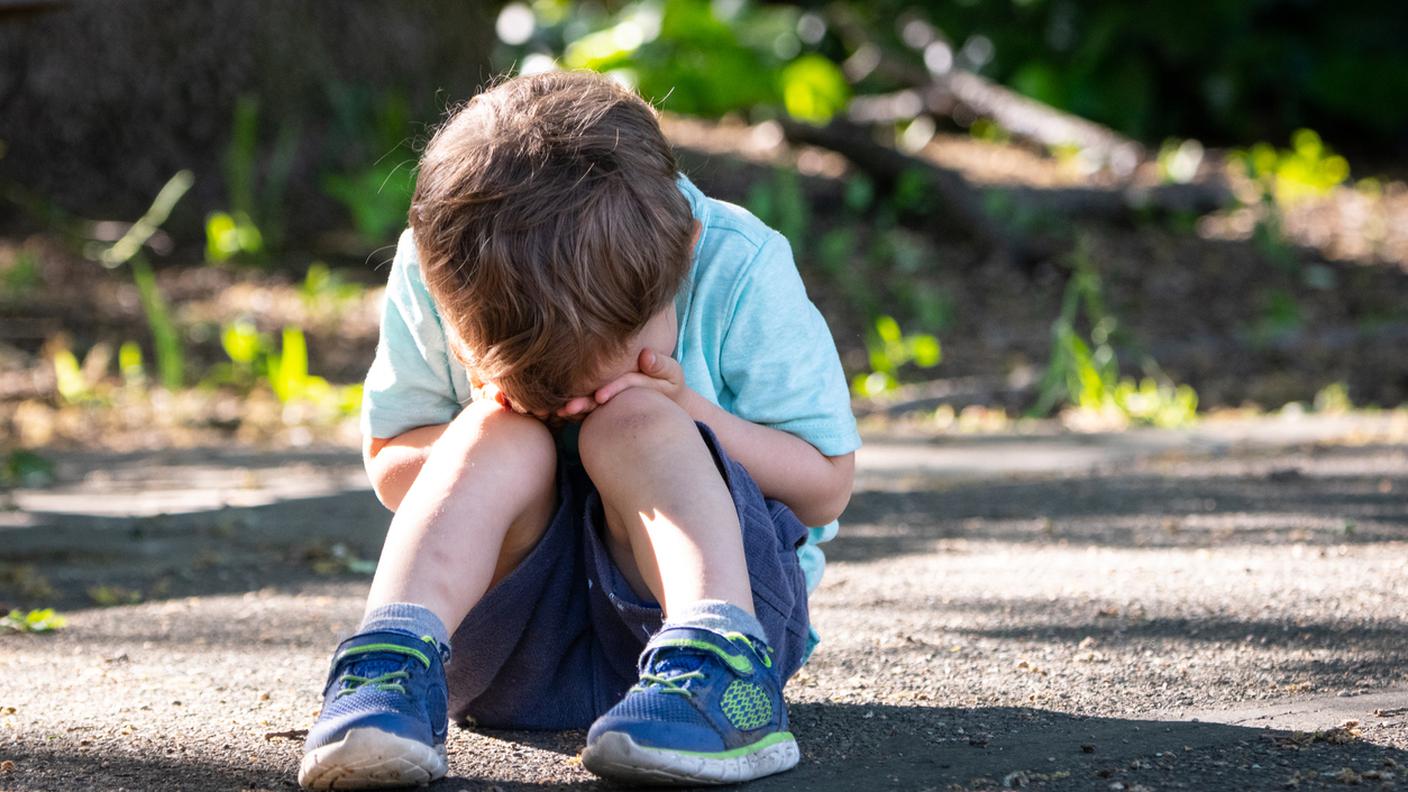 Bambino che piange seduto sul pavimento coprendo il suo viso