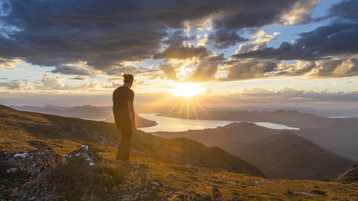 Uomo in piedi sulla scogliera a guardare il tramonto sulla catena montuosa dorata