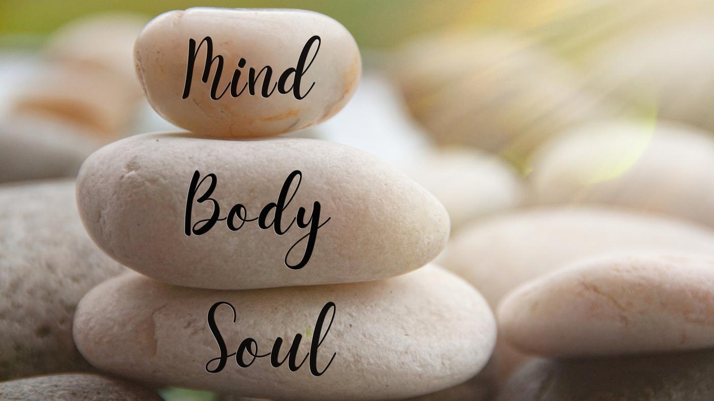Luce splendente sulle pietre zen con le parole Mente, Corpo, Anima su sfondo sfocato